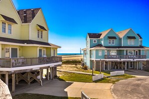 Une propriété située en bord de mer, comprenant des maisons à plusieurs étages, une terrasse en bois et une vue dégagée sur l’océan.