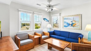 Ein modernes Wohnzimmer mit einem blauen Sofa, Holzmöbeln und großen Fenstern mit Blick ins Freie.