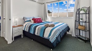 A bedroom with a bed, a nightstand, a lamp, an air conditioning unit, a window with a view, and a metal shelf with plants. - Spacious Esplanade Apartment With Rooftop Access (Hervey Bay)