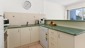 A kitchen with white cabinets, a green countertop, a microwave, a coffee maker, and a clock on the wall. - Spacious Esplanade Apartment With Rooftop Access (Hervey Bay)