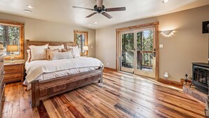 Un dormitorio con cama de madera, ventilador de techo y un ventanal con vistas a árboles.
