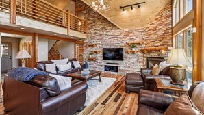 Un amplio salón con chimenea de pared de piedra, sofás de cuero y televisor montado en la pared.