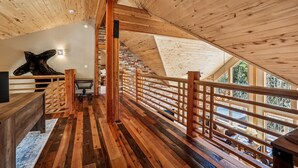 Un interior de madera con techo inclinado, una escalera que conduce a un nivel superior y una gran escultura de cabeza de madera en la pared.