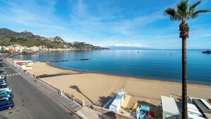 A coastal view with a beach, a palm tree, and a road with parked cars. - Sea Escape - Apartment by the Sea (Giardini Naxos)