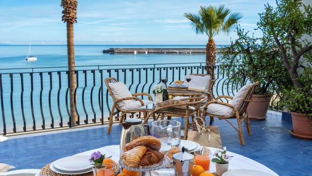 A table set for breakfast with wicker chairs, a view of the sea, and a railing. - Sea Escape - Apartment by the Sea (Giardini Naxos)