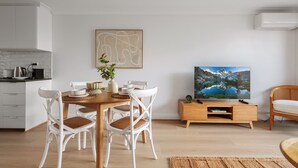 Uma sala de estar moderna com uma mesa de jantar de madeira, cadeiras de vime branco, uma TV de tela plana e um armário de madeira.