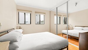 A bedroom with a large bed, a mirror, and two windows. - Lovely 2-bed With Balcony (Sydney)