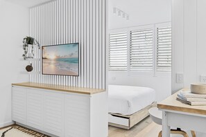 Ein modernes Schlafzimmer mit einem Bett, einem Nachttisch, einem Fenster mit Jalousien, einem an der Wand befestigten Regal mit einer Pflanze und einem gerahmten Bild.