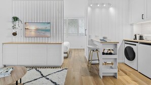 A modern kitchen with white cabinetry, a built-in washing machine, and a dining area with a wooden table and chairs. - Studio4: Bondi Chic Interiors With Rooftop Pool (Sydney)