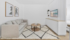 A modern living room with a sofa, a coffee table, and a TV mounted on a wall with a striped pattern. - Studio4: Bondi Chic Interiors With Rooftop Pool (Sydney)