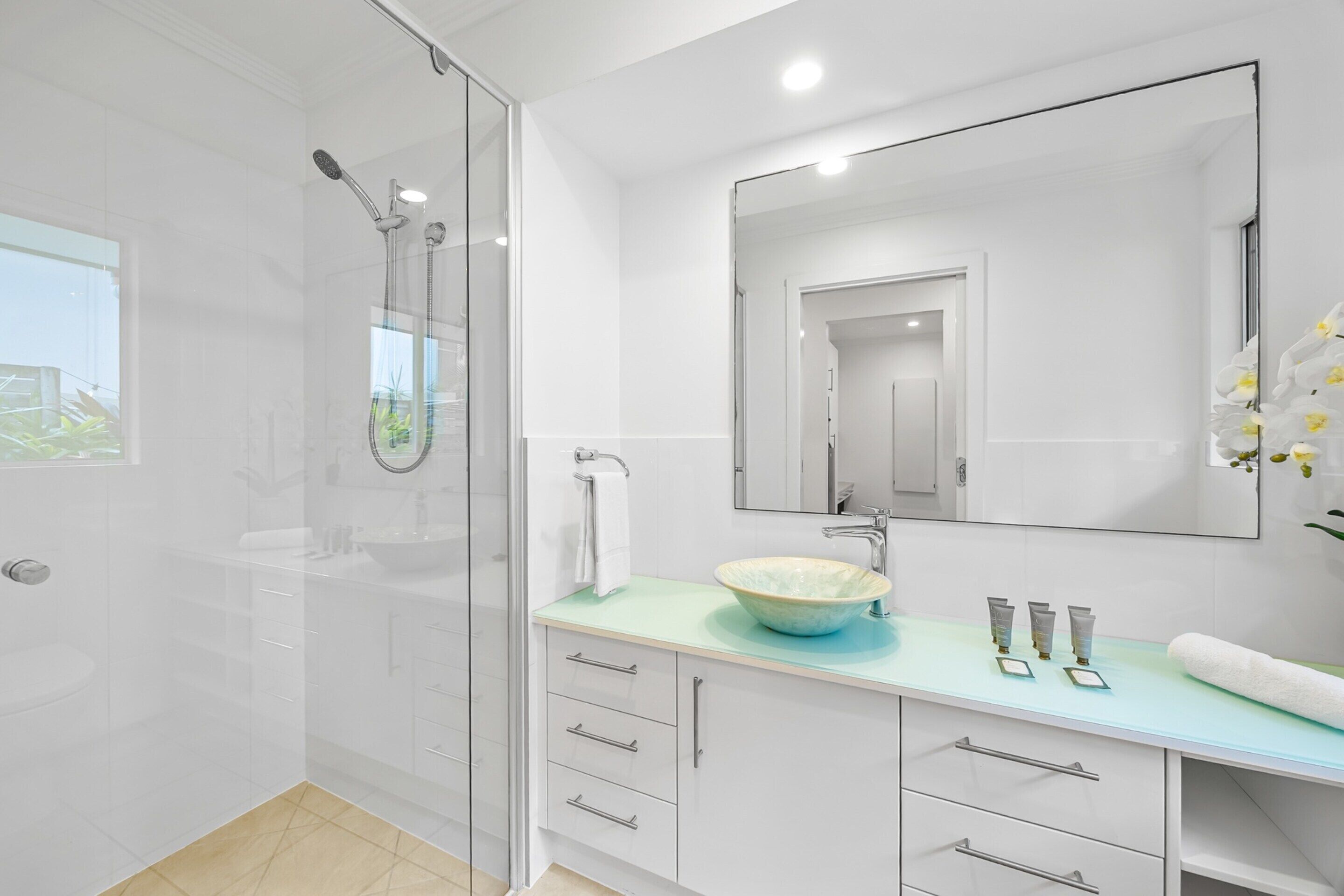 A modern bathroom with a glass shower enclosure, a white sink with a blue countertop, and a large mirror above the sink.