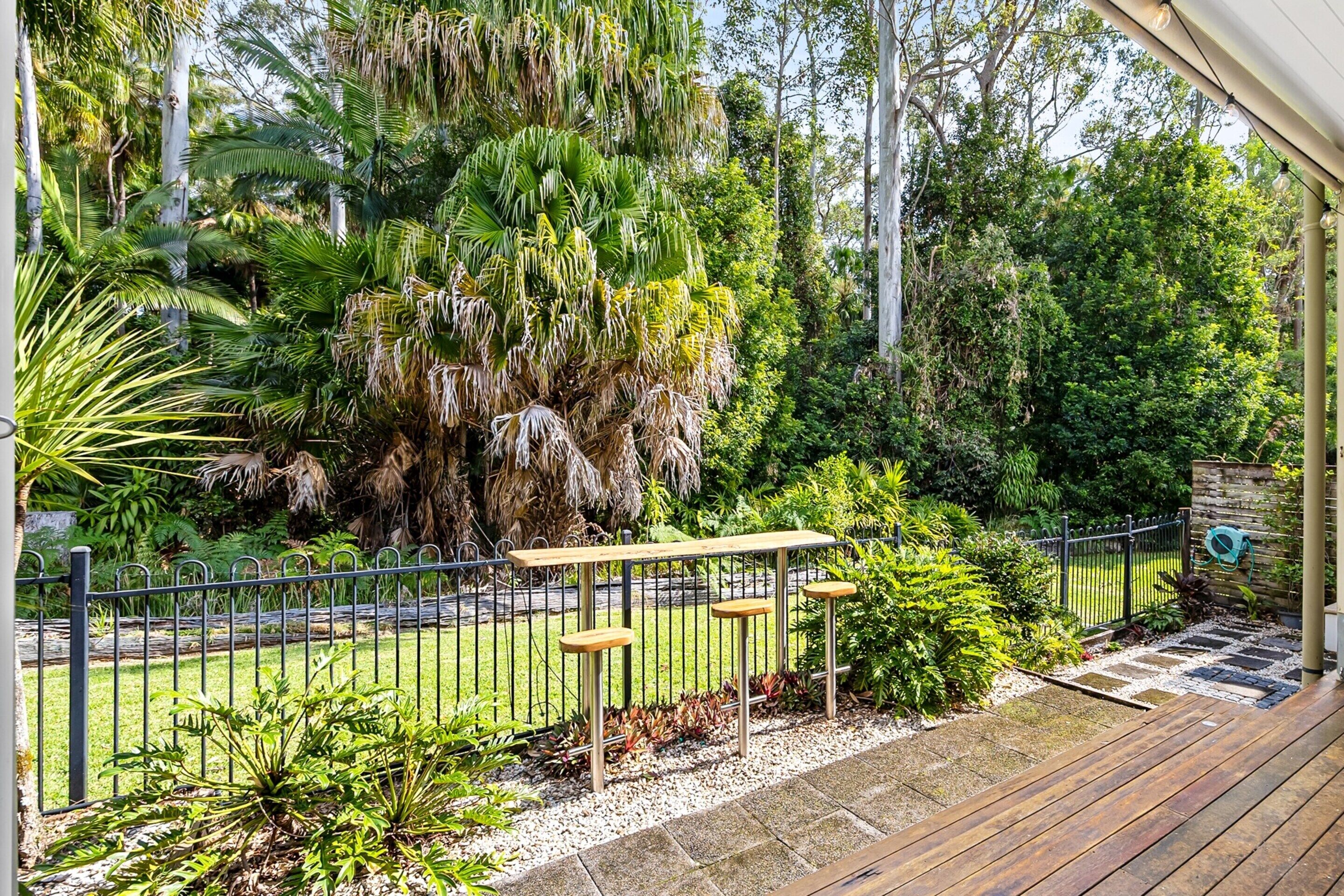 A garden with a wooden deck, a metal fence, and various plants.