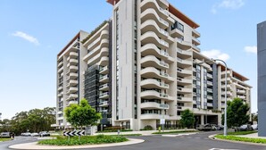 A multi-story residential building with balconies, a landscaped area with trees, and a clear sky. - Luxe 2-bed: Modern Interiors, Balcony & BBQ Area (Sydney)