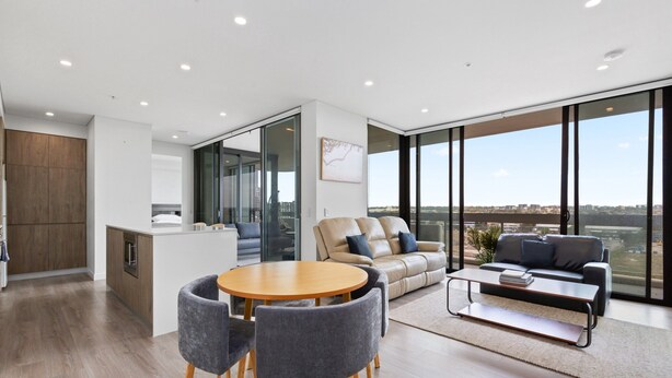 A modern living space with a dining area, sofa, and large windows offering a city view. - Luxe 2-bed: Modern Interiors, Balcony & BBQ Area (Sydney)