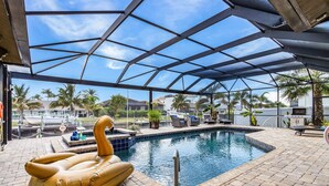 Una piscina techada con un jacuzzi, sillas de descanso y palmeras al fondo.