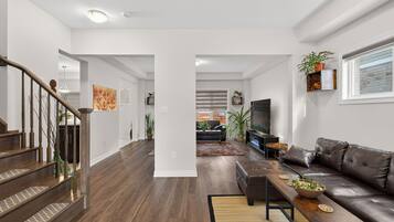 Una sala de estar moderna con una escalera, un sofá de cuero, una mesa de centro y una televisión.