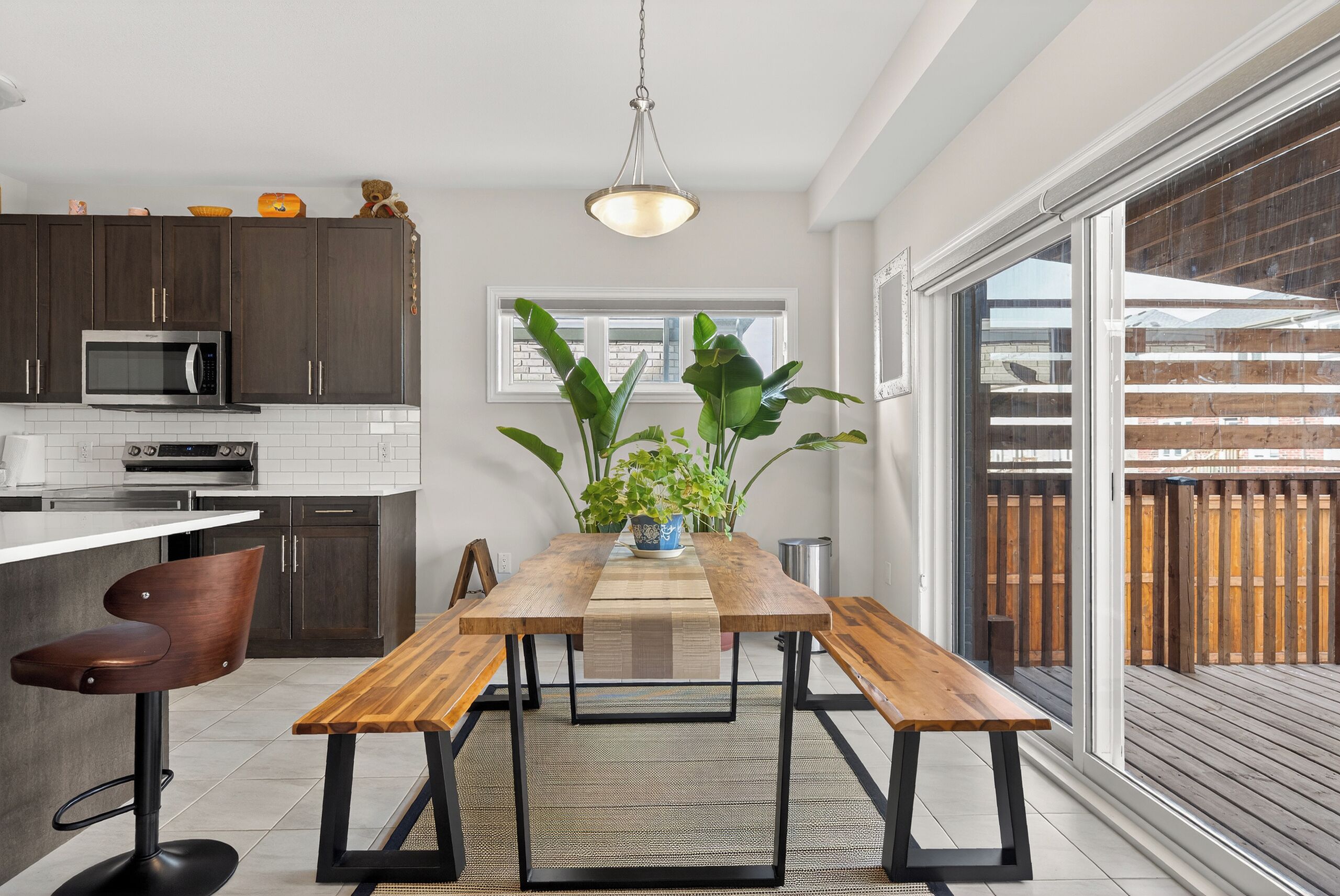 Una cocina moderna con armarios oscuros, un microondas de acero inoxidable, una mesa de comedor de madera con bancos y una lámpara colgante.