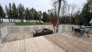 A wooden deck with a table and chairs, a small play area, and a view of a lake and forest. - Lakefront 2-BR Cottage Retreat in Kagawong - Lilly Lakehouse (Billings)