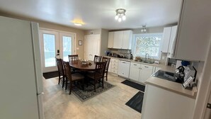 A kitchen with a dining table, chairs, cabinets, a refrigerator, and a window. - Lakefront 2-BR Cottage Retreat in Kagawong - Lilly Lakehouse (Billings)