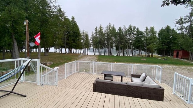 A deck with a wicker sofa, a small table, and a hammock. - Lakefront 2-BR Cottage Retreat in Kagawong - Lilly Lakehouse (Billings)