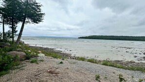 A rocky shoreline with a view of a calm sea and a distant forested island. - Lakefront 2-BR Cottage Retreat in Kagawong - Lilly Lakehouse (Billings)