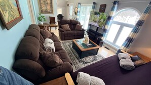 A living room with a brown sofa, a glass coffee table, and a TV. There is a window with curtains and a painting on the wall. - Lakefront 2-BR Cottage Retreat in Kagawong - Lilly Lakehouse (Billings)