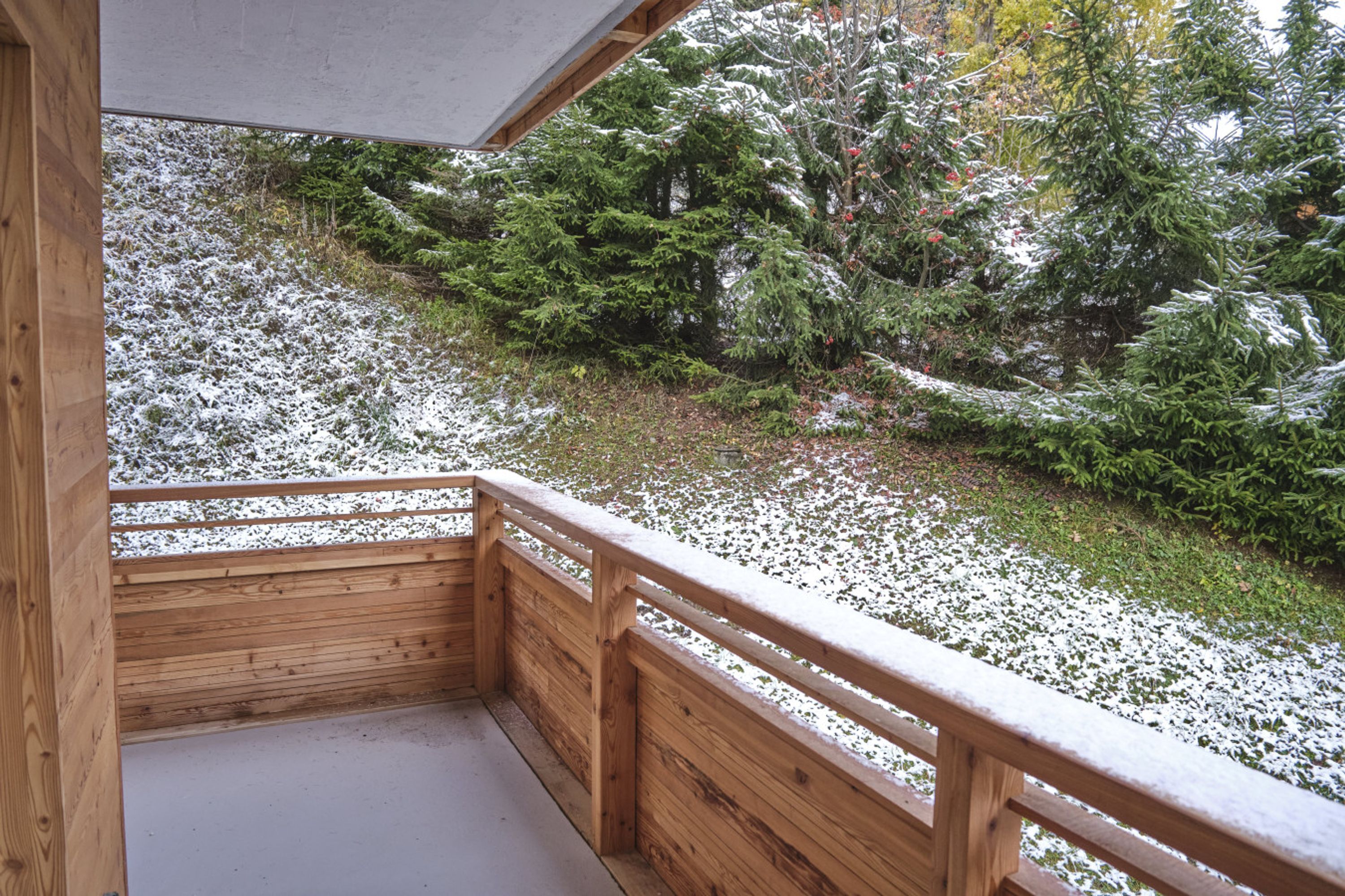 Un balcón de madera con vistas a terreno nevado y árboles de hoja perenne.
