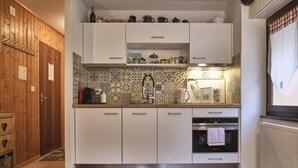 A kitchen with white cabinets, a tiled backsplash, and a stove. - Studio Pierre a Voir 4 (Riddes)