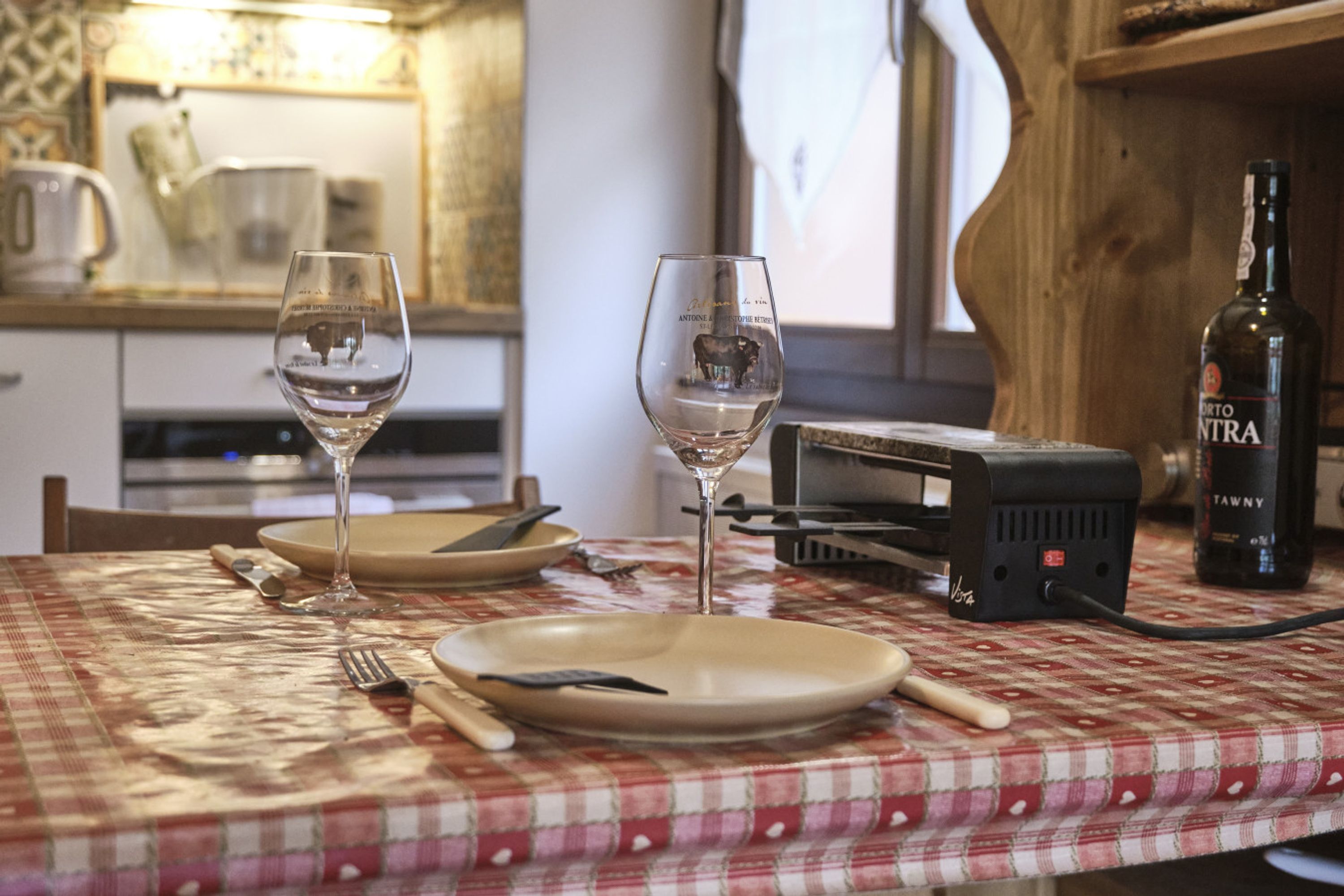 A dining table with two wine glasses, plates, cutlery, and a bottle of wine.