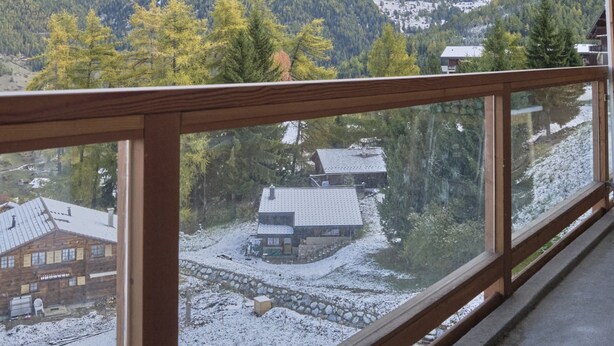 A view from a balcony with a wooden railing, overlooking a snow-covered landscape with mountains and trees. - Cosy Apartment in the Centre of Town With Views and Parking (Riddes)
