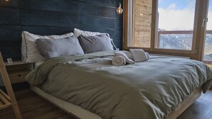 A bedroom with a bed, pillows, a rolled towel, a nightstand, and a window with a view of mountains. - Cosy Apartment in the Centre of Town With Views and Parking (Riddes)