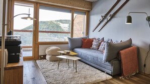 A cozy living room with a grey sofa, wooden floor, and a large window offering a view of a mountainous landscape. - Cosy Apartment in the Centre of Town With Views and Parking (Riddes)