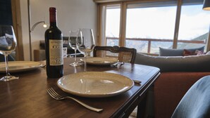 A dining table with a wine bottle, glasses, and plates, set in a room with a window and a sofa. - Cosy Apartment in the Centre of Town With Views and Parking (Riddes)