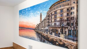 A large painting of a waterfront cityscape with buildings and a tower.