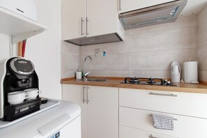 A compact kitchen with a coffee machine, a sink, and a stove.