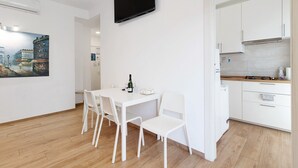 A modern kitchen with white cabinets, a flat-screen TV, and a dining area with a white table and chairs.