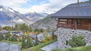 A mountain lodge with stone walls and a wooden balcony, overlooking a valley with snow-capped mountains and a small town. - Beautiful Luxury Chalet Veyon With Incredible Views (Riddes)