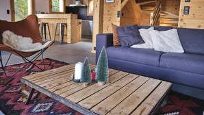 A cozy living room with a blue sofa, a wooden coffee table with candles and a Christmas tree, and a brown leather chair. - Beautiful Luxury Chalet Veyon With Incredible Views (Riddes)
