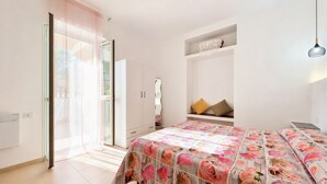 Quarto com cama, guarda-roupa, estante com objetos decorativos e luminária pendente.