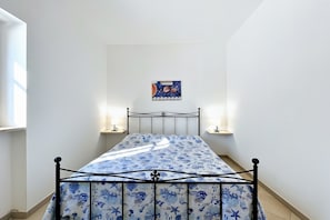 Una cama con estructura metálica y colcha azul con estampado floral, dos lámparas de noche, un reloj en la pared y un pequeño cartel en la pared.
