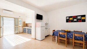 A modern kitchen with a refrigerator, a dining table with chairs, and a TV mounted on the wall. - Apartment 'Francesca, Trilo A' with Shared Terrace, Wi-Fi and Air Conditioning (Peschici)