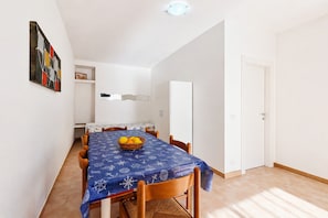 Un coin repas avec une table dressée pour quatre personnes, un saladier de fruits et un tableau accroché au mur.