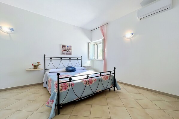 Un dormitorio con una cama, una ventana, un aire acondicionado y un estante fijado a la pared.