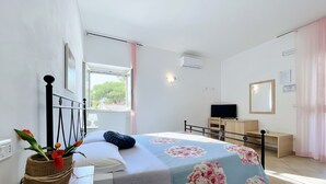 A bedroom with a bed, a desk, a television, and a window with curtains.