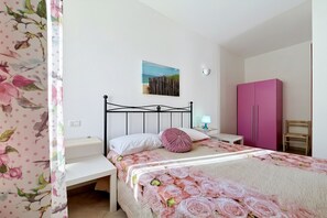A bedroom with a bed, nightstand, lamp, and a pink wardrobe.