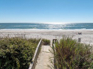 Un sentier qui longe la plage et mène au rivage, avec une clôture en bois et de la végétation de chaque côté.
