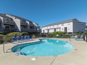 Une piscine avec des chaises longues, un panneau indiquant qu’il est interdit de plonger, et des bâtiments à deux étages en arrière-plan.
