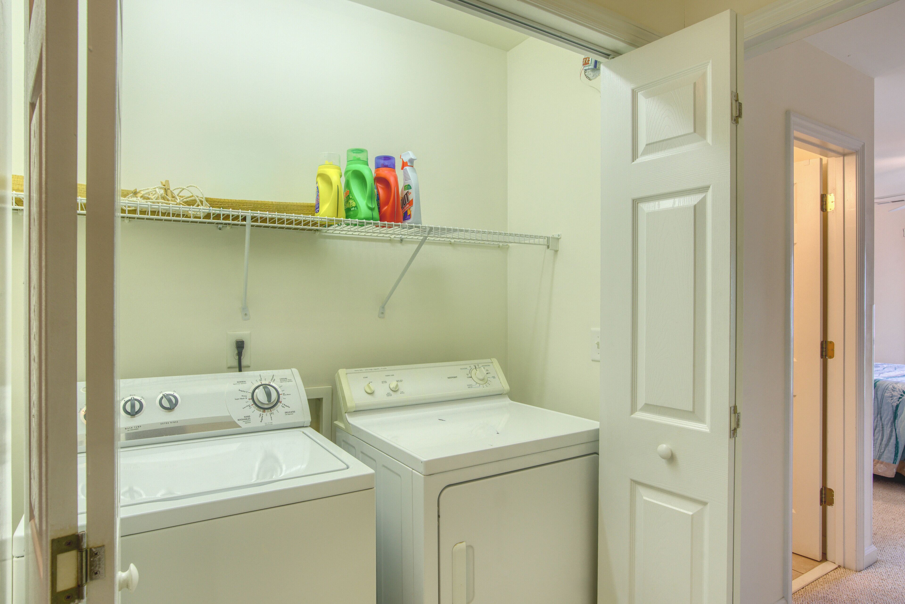 A laundry room with two washers and dryers, a shelf with detergent bottles, and a door leading to another room.