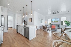 A modern kitchen with a central island, pendant lighting, and a dining area with wooden furniture.