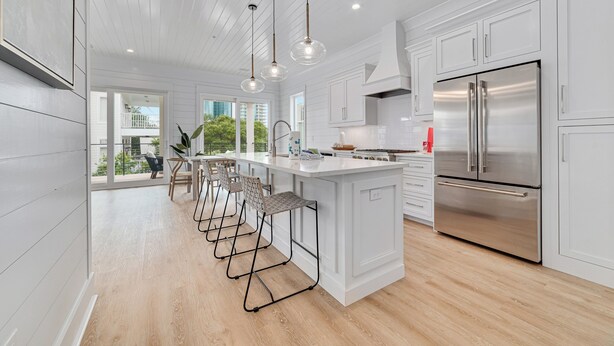 A modern kitchen with white cabinetry, a stainless steel refrigerator, pendant lights, and a bar area with stools. - Luxury 5BR, Pool, Walk To Beach, Private Boat Slip & Fishing Pier, Sleeps 15 (Orange Beach)